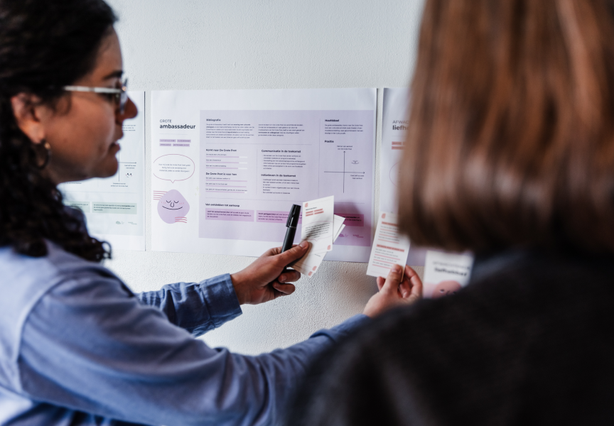 Two women looking at papers on a wall and adding postits 