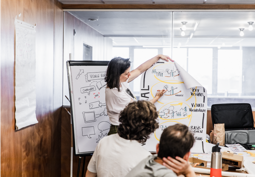 A woman presenting a poster in a meeting with colleagues